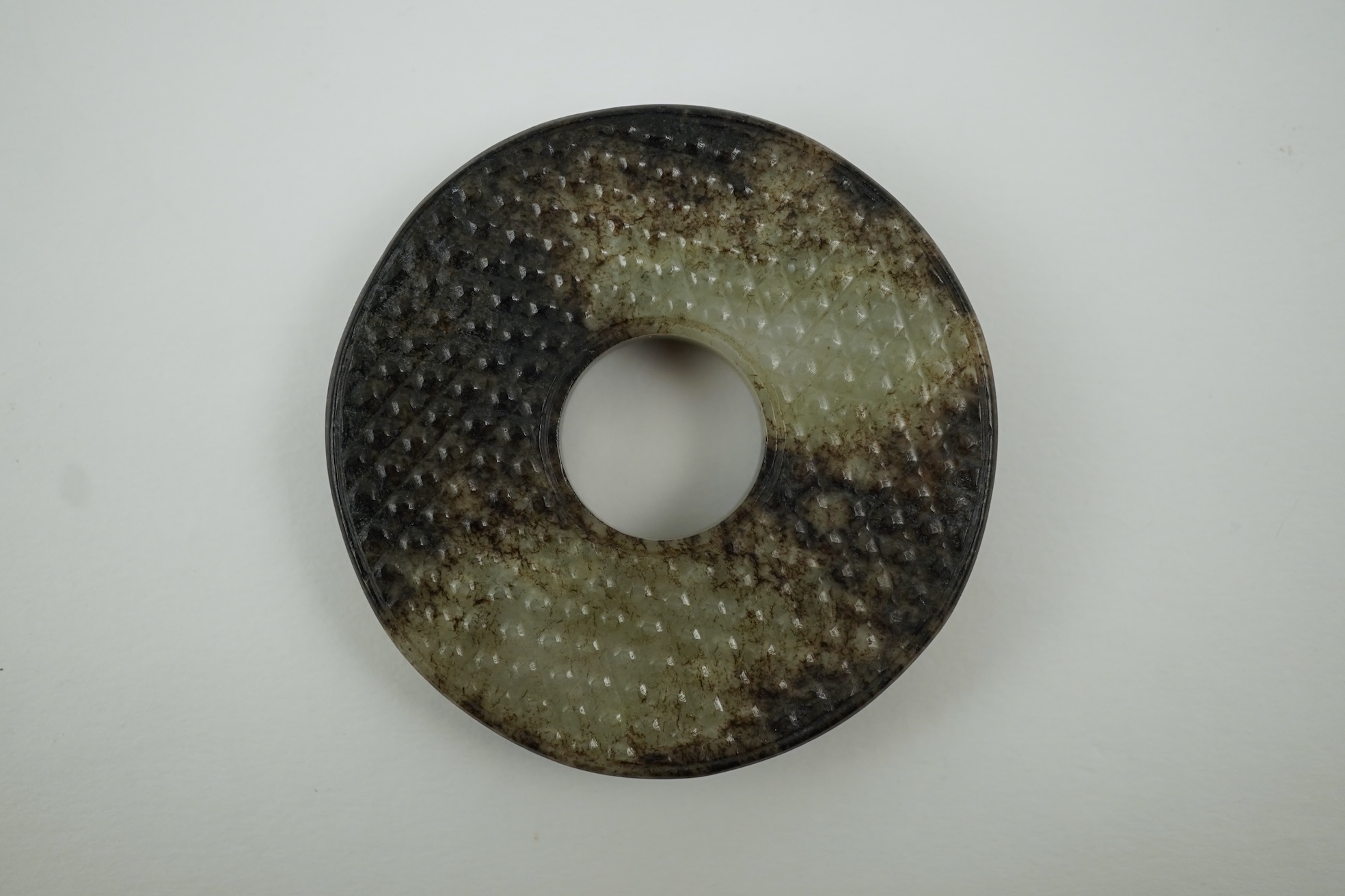 A Chinese pale celadon and black jade bi disc